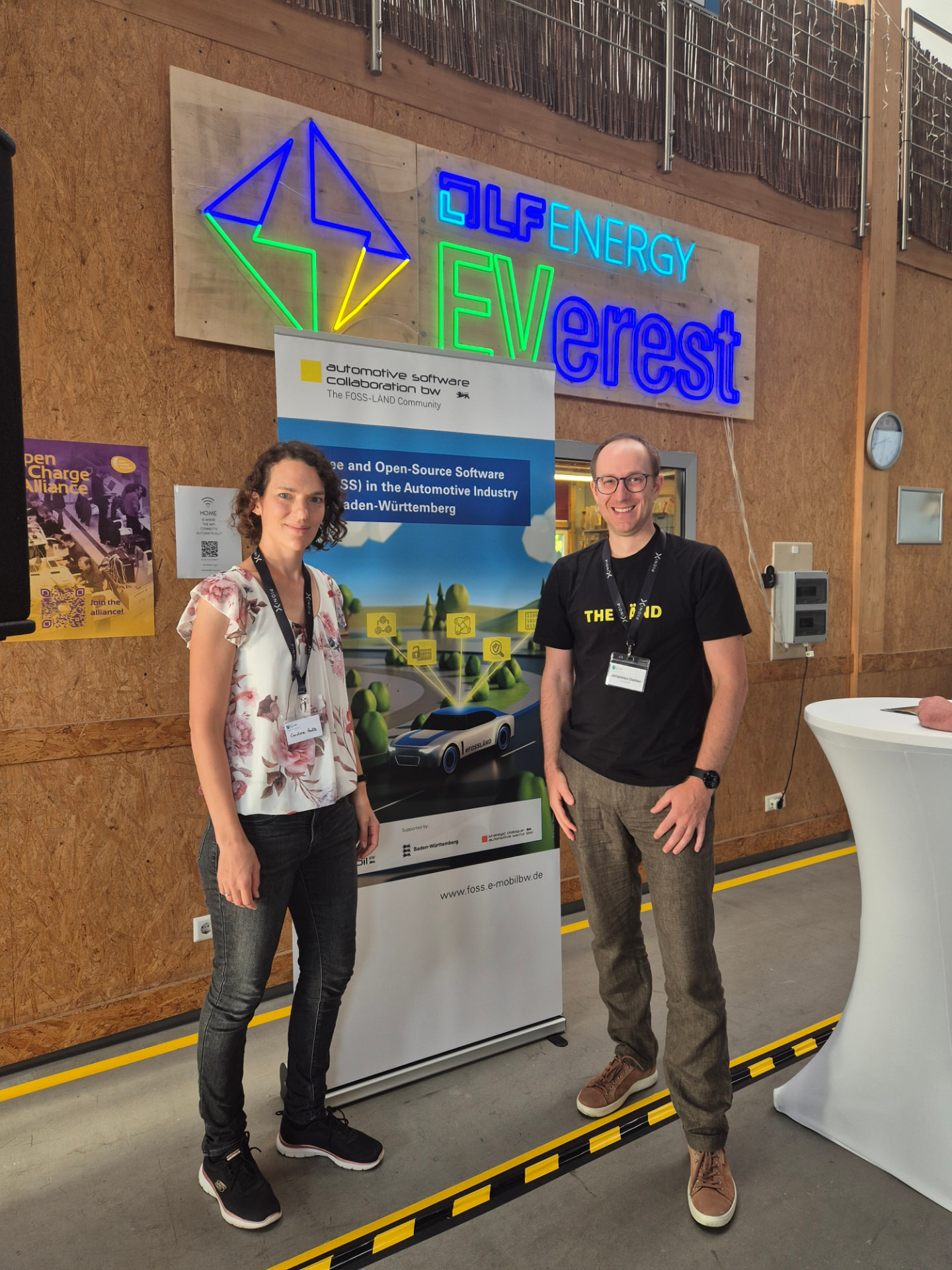 Two attendees in front of the LF Energy EVerest neon sign and the FOSS-LÄND banner